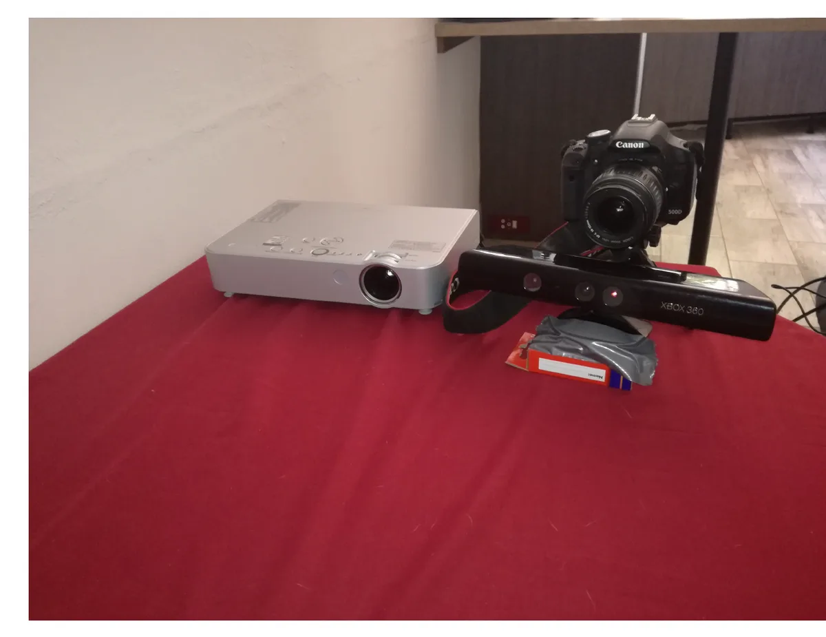 The projector, Canon 500D DSLR and Kinect for Xbox 360 mounted together on a stand, on a red tablecloth